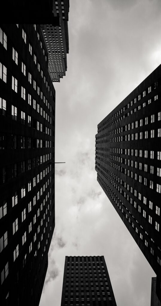 Vertical Low Angle Grayscale City Buildings With Cloudy Sky Background E1675240691587